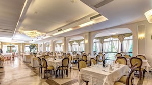A spacious dining area with multiple tables and chairs, large windows with curtains, and a high ceiling with recessed lighting. - Villa Romita (Massa Lubrense)