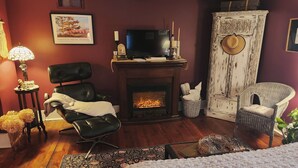 A cozy room with a fireplace, a television, a comfortable chair, and a decorative wall. - Applesauce Inn B&B (Bellaire)