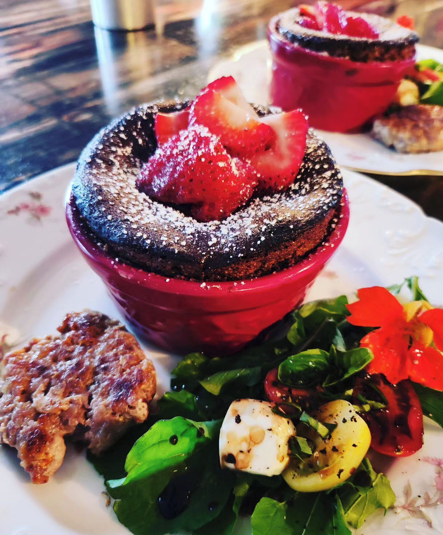 A dessert with strawberries and powdered sugar, a grilled meat dish, and a salad with greens and tomatoes.