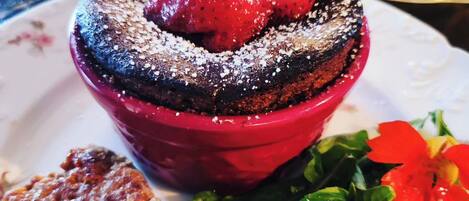 A dessert with strawberries and powdered sugar, a grilled meat dish, and a salad with greens and tomatoes.