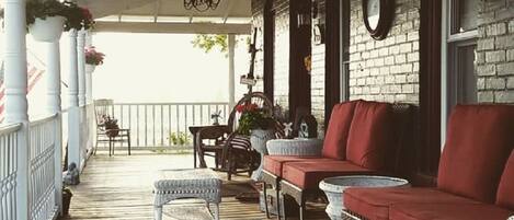 A covered porch with wooden flooring, wicker furniture, and a white railing.