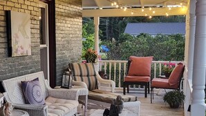 A covered porch with wicker furniture, a red rug, and string lights. - Applesauce Inn B&B (Bellaire)