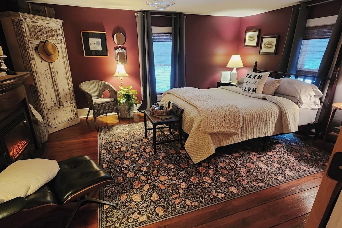 A bedroom with a bed, a chair, a table, a wardrobe, and a window.