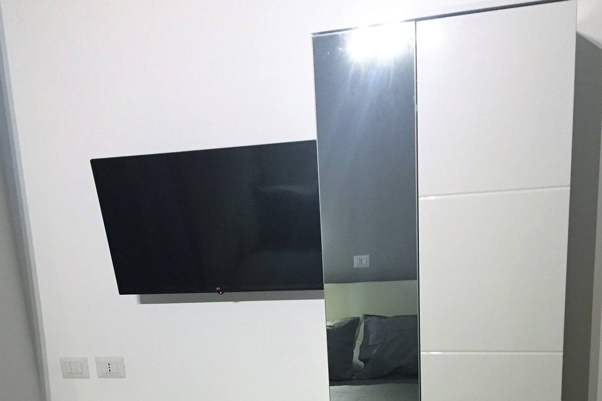 A compact room with a foldable desk, a chair, a TV mounted on the wall, and a bed with a mattress and pillows.
