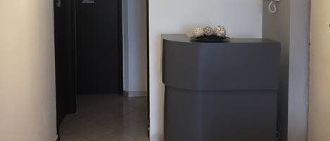 A hallway with a black door labeled '2', a grey reception desk, and a white wall with a telephone and decorative items.