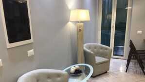 Ein Wohnzimmer mit einem Glastisch, zwei Sesseln, einer Stehlampe und einer Schiebetür aus Glas.