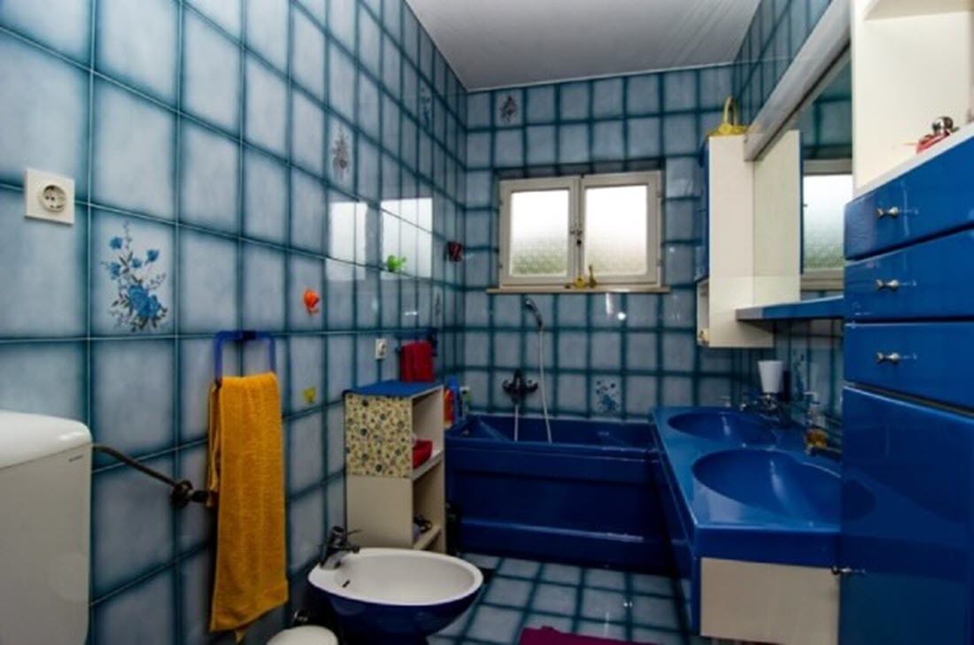 Un bany amb rajoles blaves, un lavabo blanc, una banyera blava i una finestra.