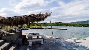 A concrete dock with a stone bench and a thatched umbrella, overlooking a calm body of water with a distant shoreline. - Apartmani MAK (Korcula)
