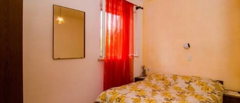 Een slaapkamer met een bed, een spiegel, een raam met rode gordijnen en een plafondlamp.