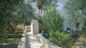 A stone pathway leading to a building with a stone wall and greenery on either side. - Apartmani MAK (Korcula)