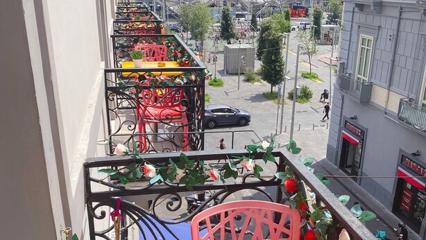 A balcony with a red chair, yellow table, and potted plants. - Dolce Vita Rooms & Breakfast (Naples)