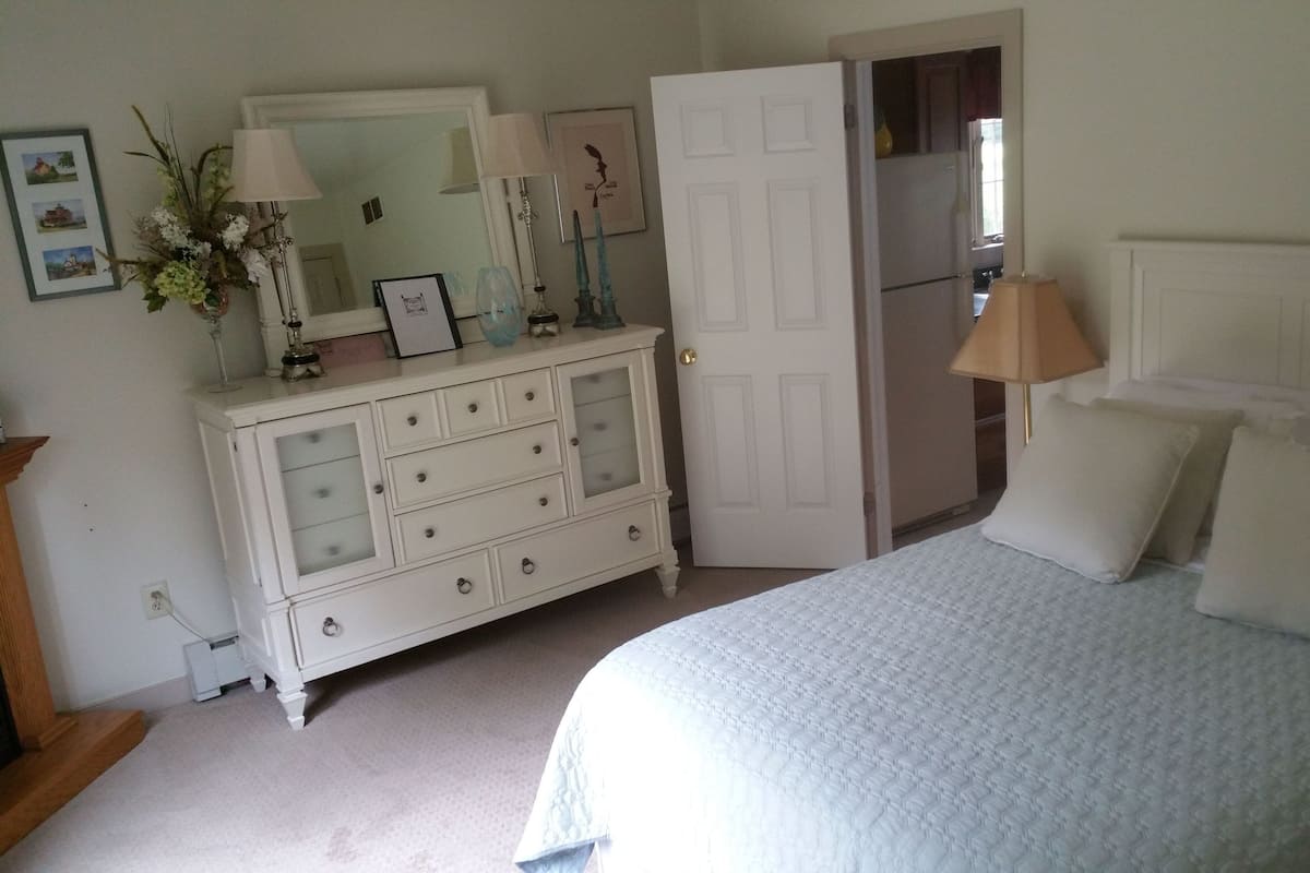 A bedroom with a bed, dresser, mirror, and a door leading to another room.
