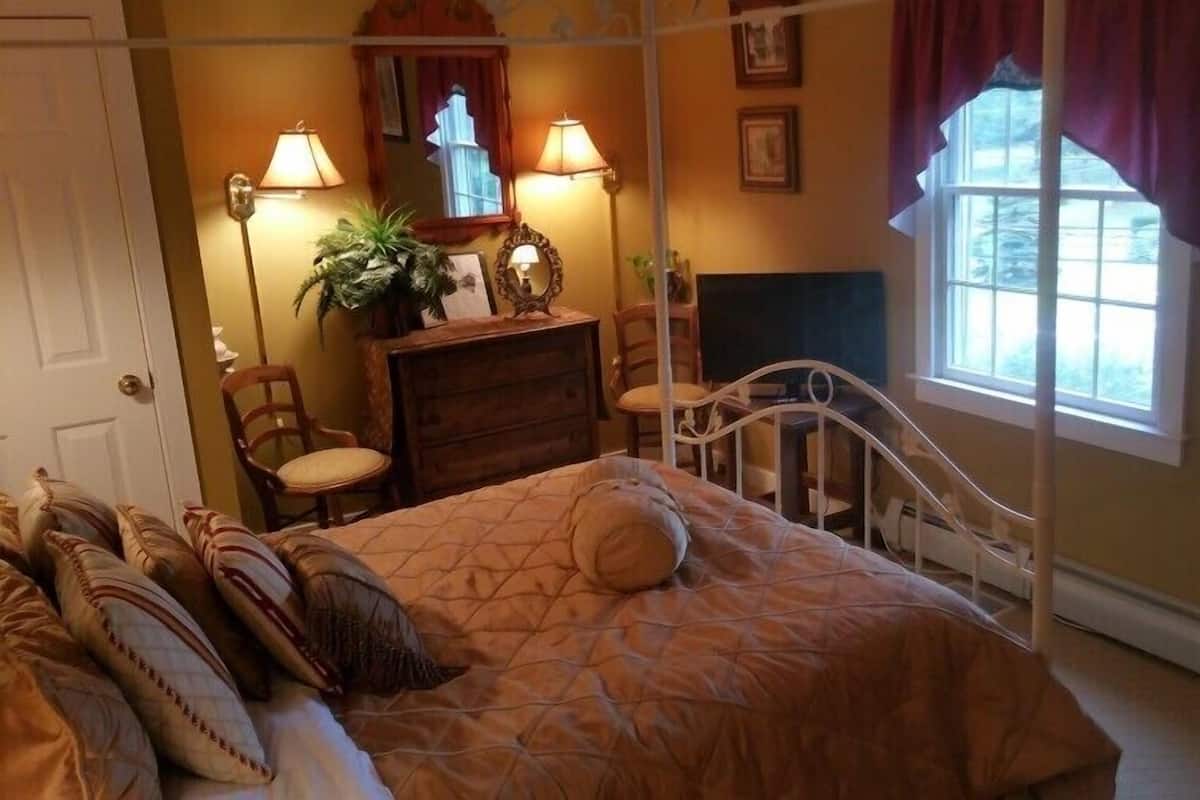 A bedroom with a bed, a dresser, a chair, a fireplace, and a window with curtains.