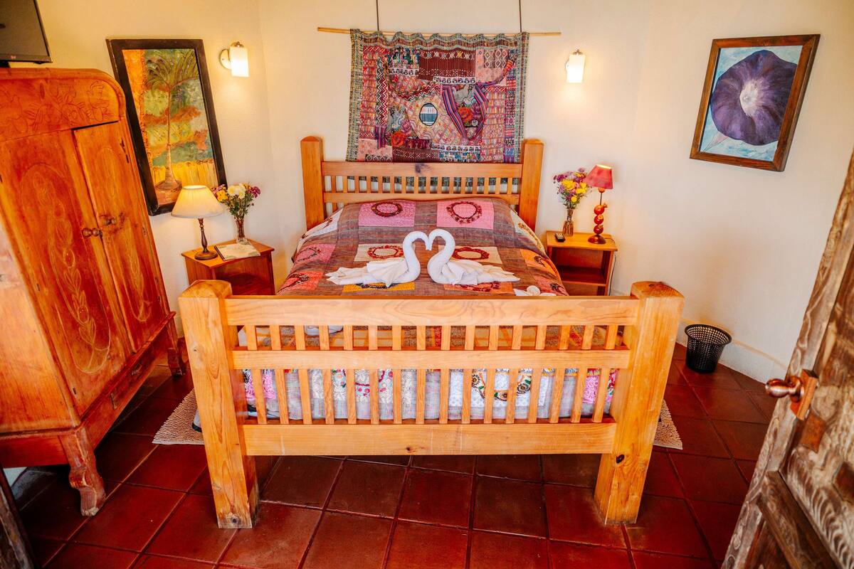 A wooden bed with a quilt featuring swans, a tapestry, and wall art.