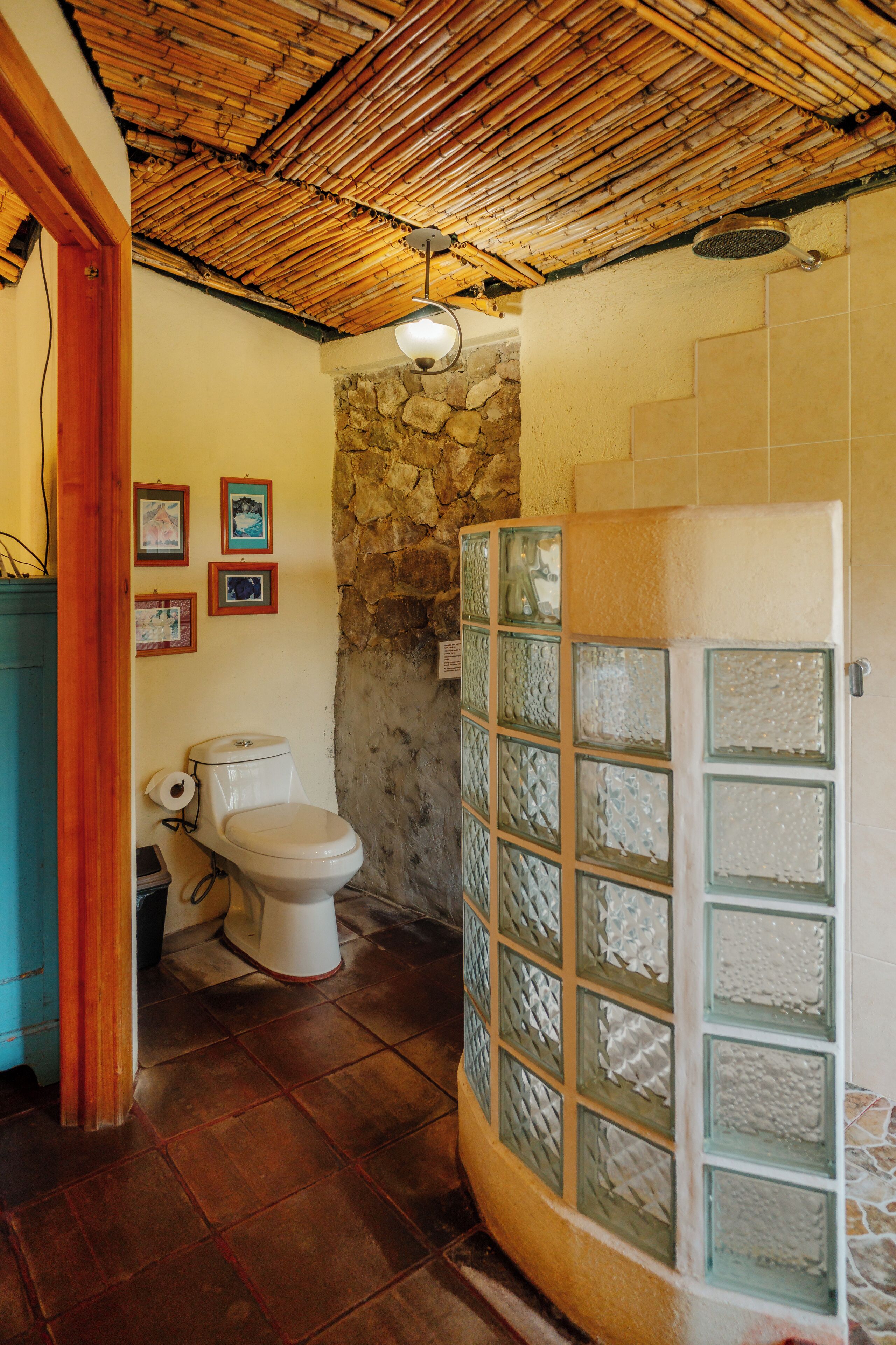 A bathroom with a bamboo ceiling, a stone wall, and a glass shower enclosure.