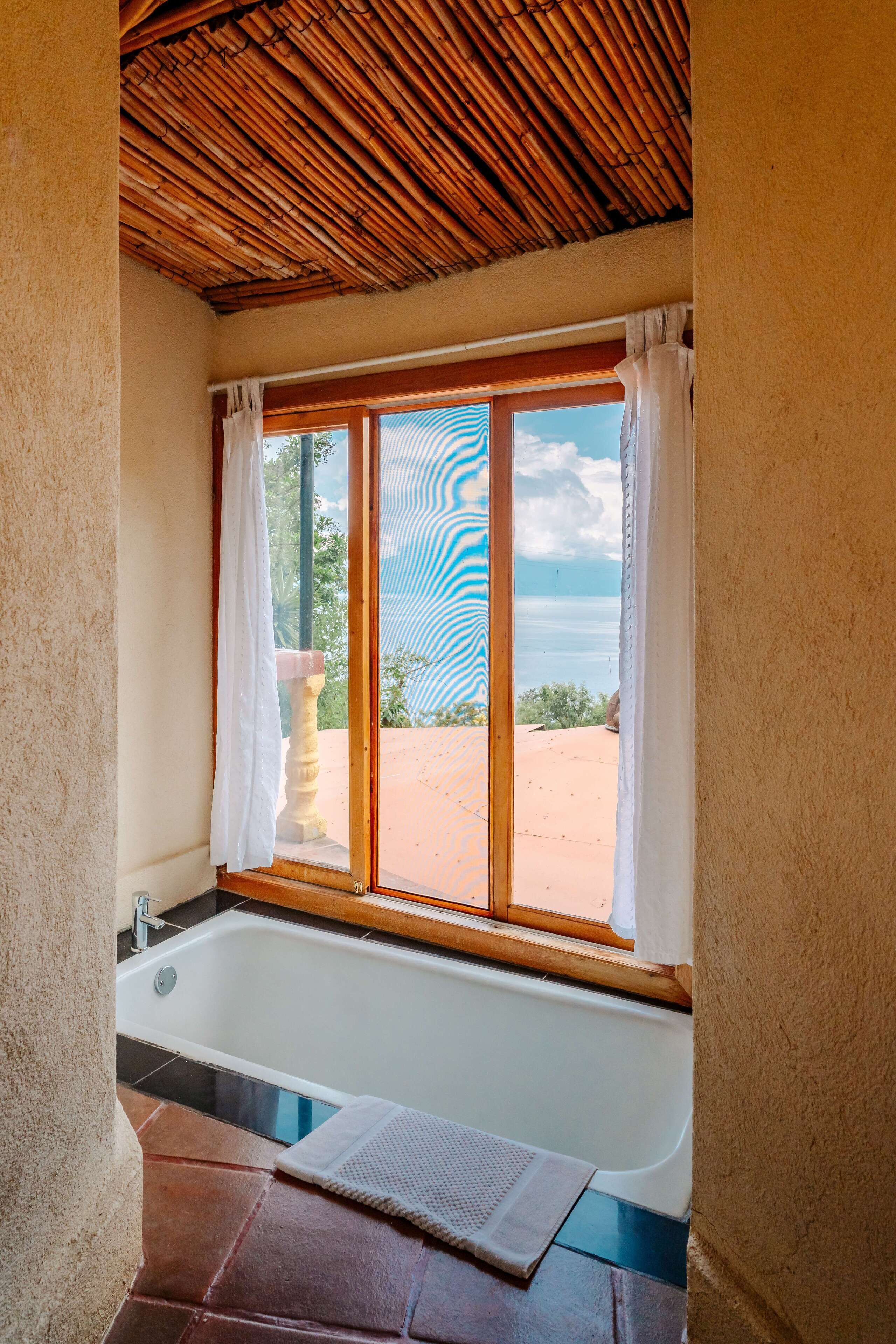 Un baño con bañera, ventana con vista a la playa y techo de madera.
