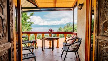 Un balcón de madera con una mesa y sillas, con vistas a un paisaje pintoresco de un lago y montañas.