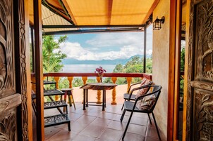 Un balcón de madera con una mesa y sillas, con vistas a un paisaje pintoresco de un lago y montañas.
