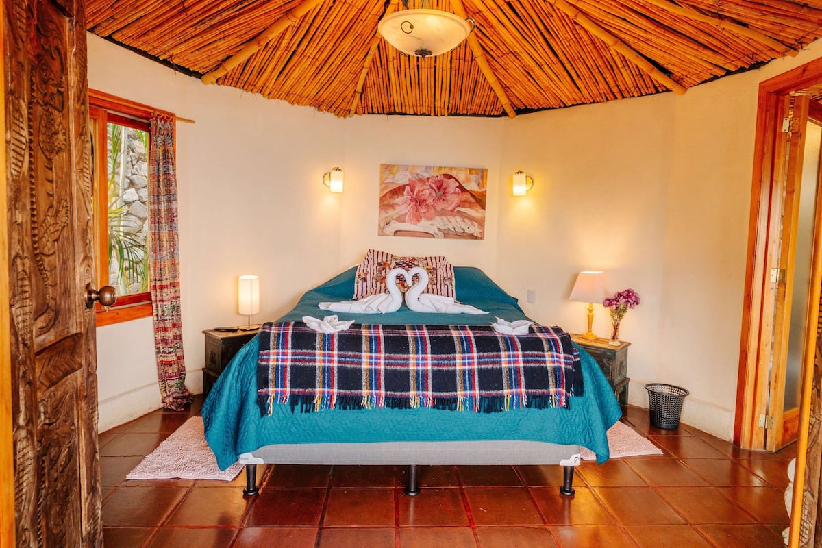 A room with a bed, a wooden ceiling, a wall painting, and two wall-mounted lights.