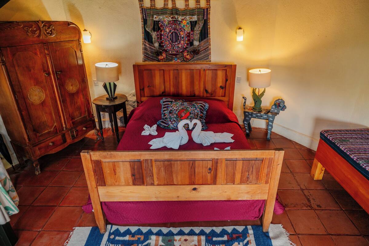 A wooden bed with a red bedspread and two wall-mounted lamps.