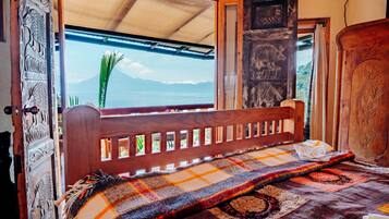 A bed with a colorful blanket, a wooden headboard, and a view of the sea through a window.