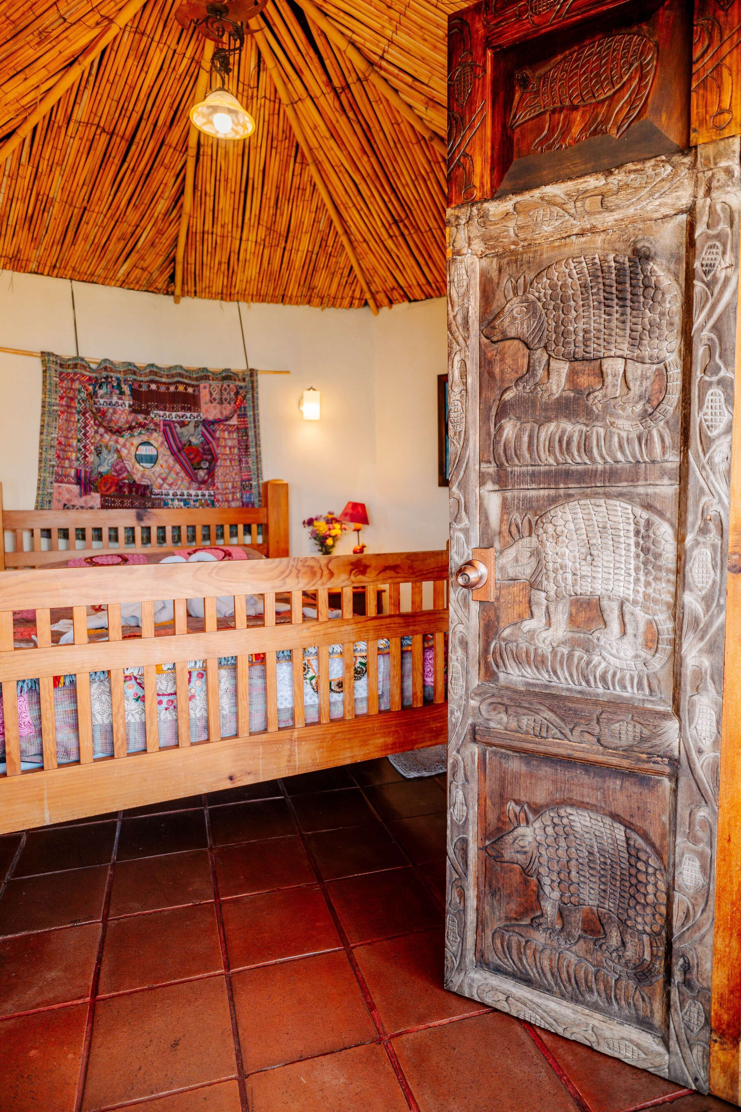 A room with a wooden door featuring ancient Egyptian carvings, a woven thatched ceiling, and a colorful tapestry on the wall.