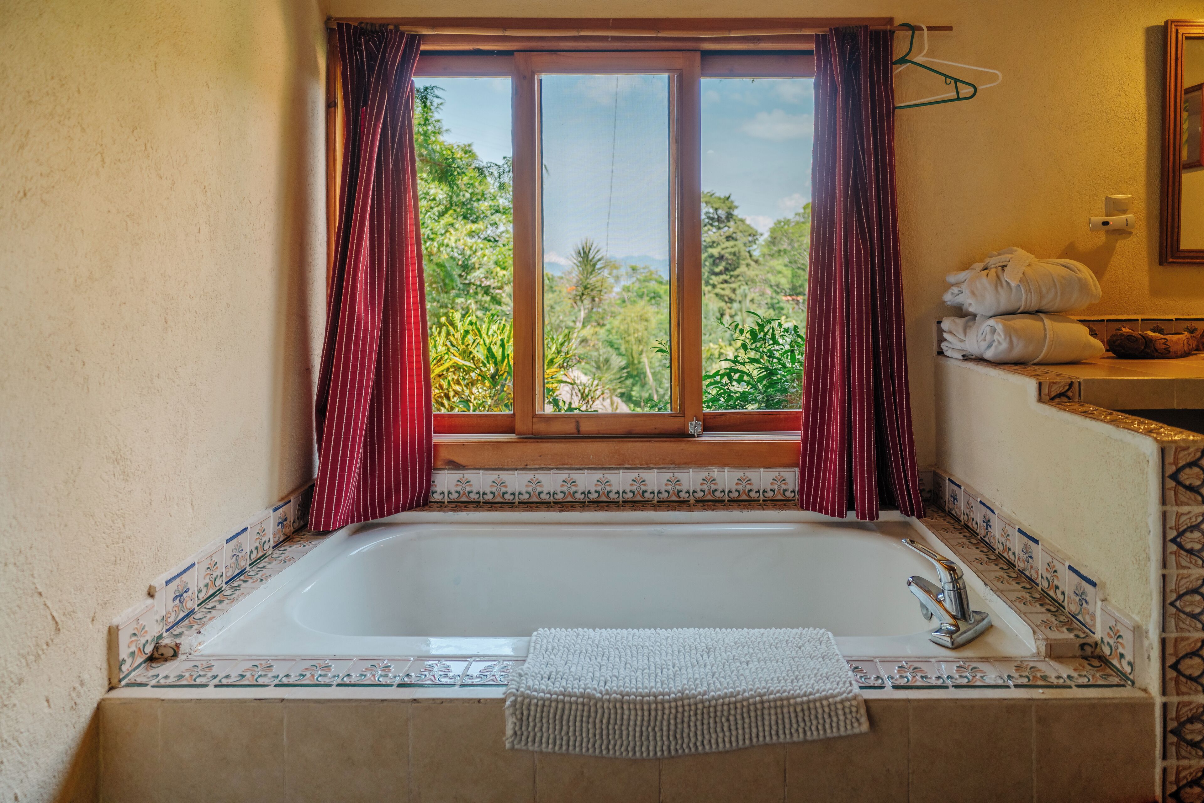 A bathroom with a bathtub, a window with curtains, and a towel rack with towels.
