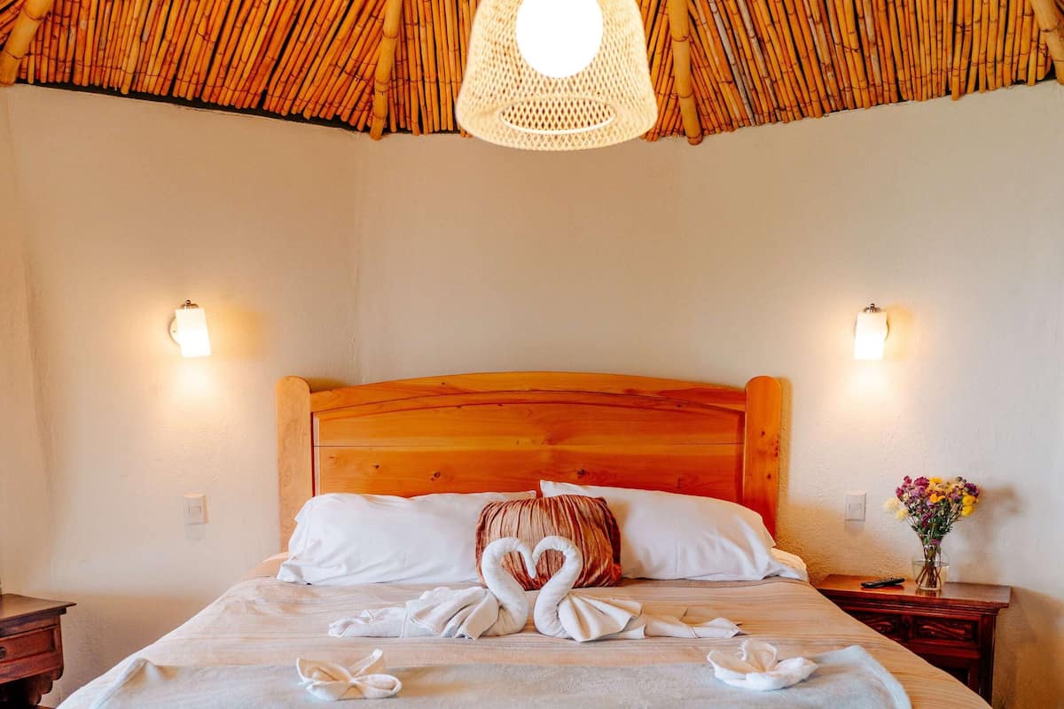 A neatly made bed with a swan-shaped towel arrangement, a wooden headboard, and a bamboo ceiling.
