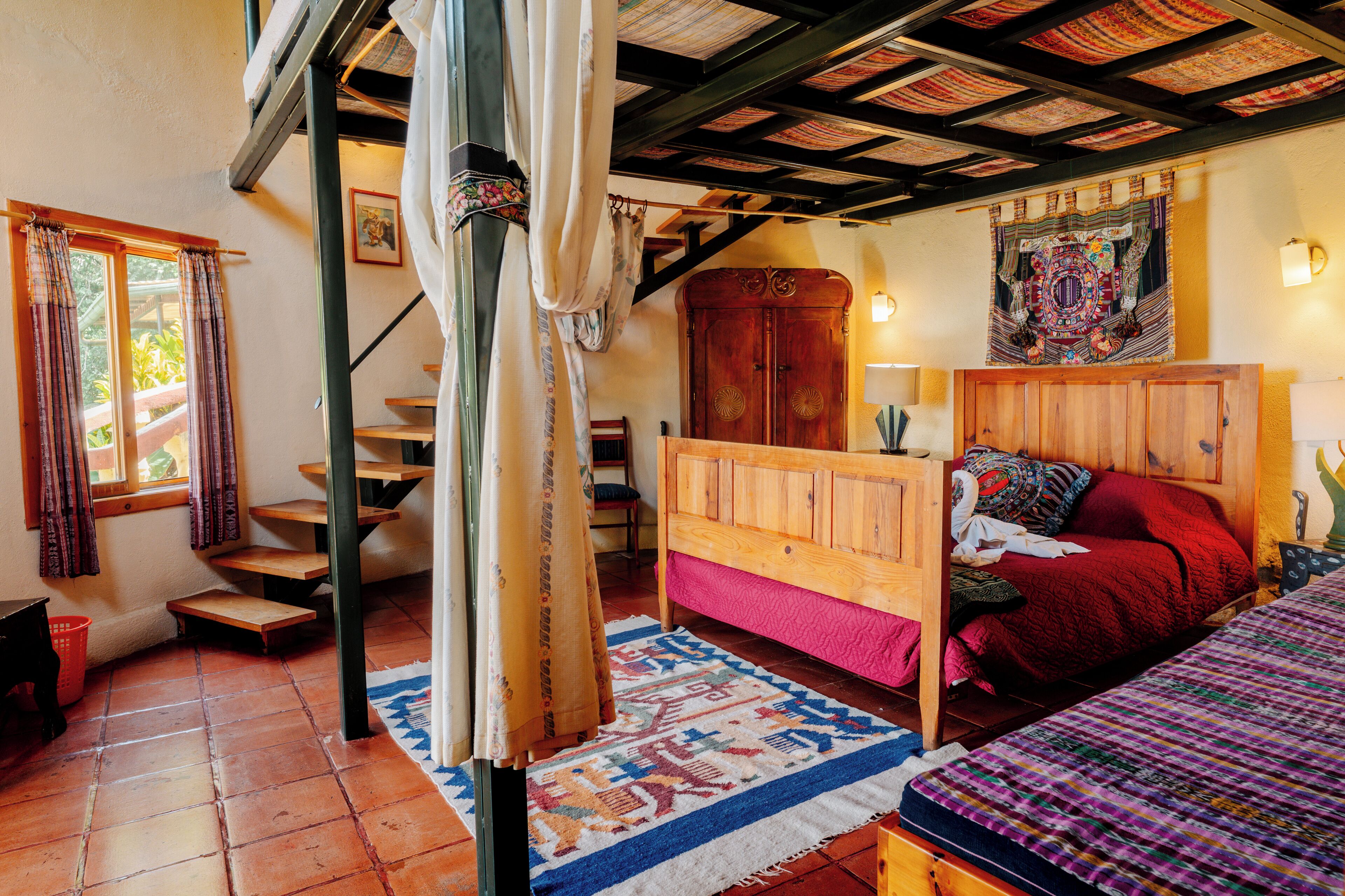 Une chambre à coucher avec un lit en bois, une couvre-lit rouge, une armoire en bois et un escalier.
