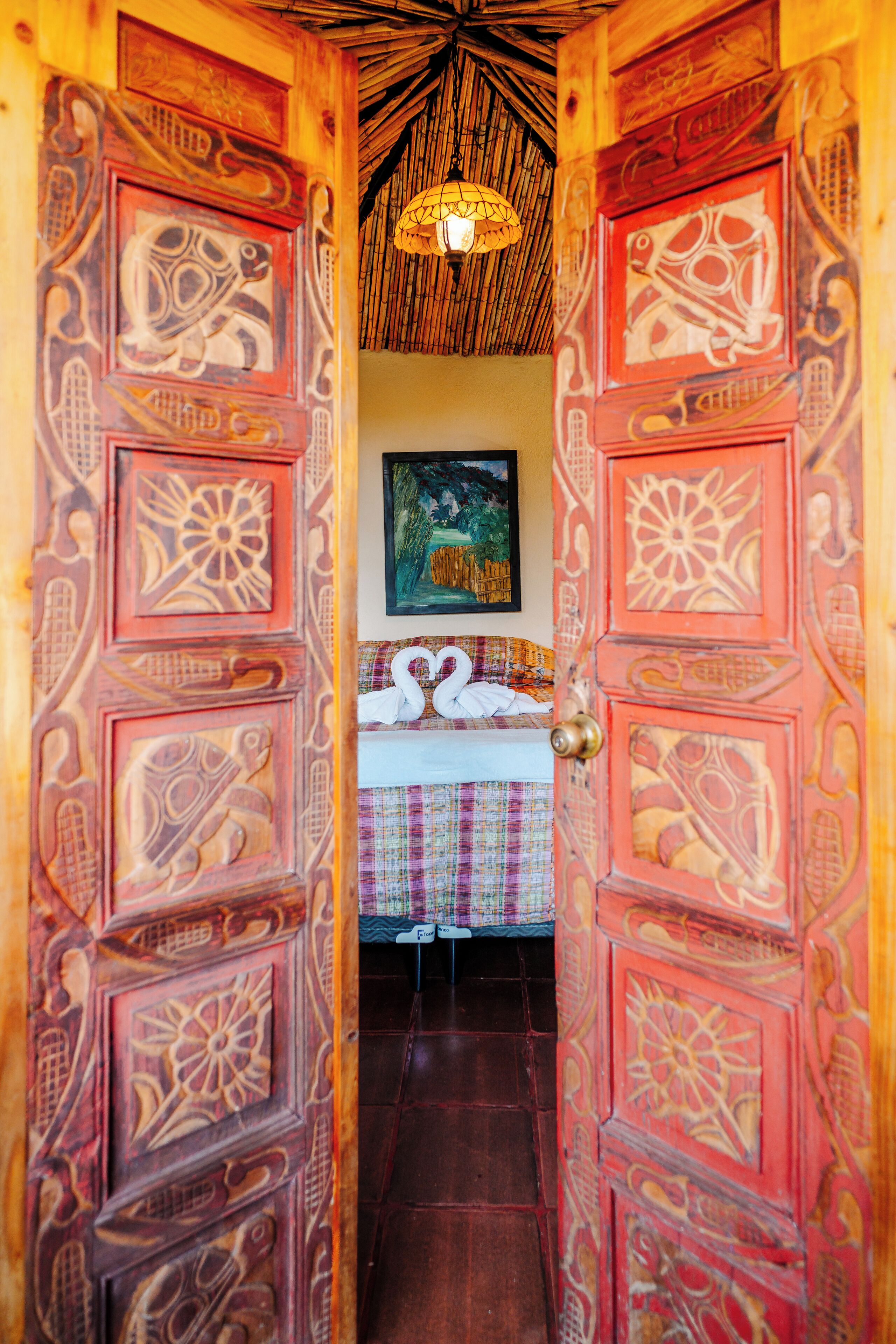Une pièce avec un lit, un tableau accroché au mur et une porte ornée de sculptures complexes.