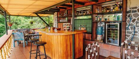 Un espace bar en bois, avec des tabourets, un comptoir et des étagères remplies de bouteilles.