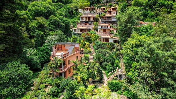 A hillside property with multiple buildings, including a prominent house with a spiral staircase and a smaller structure with a red roof.