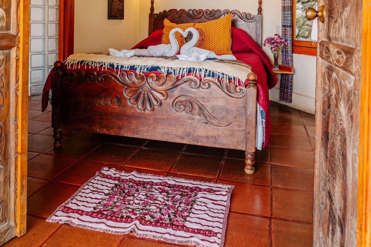 A room with a bed, a wooden ceiling, a painting on the wall, and a door.