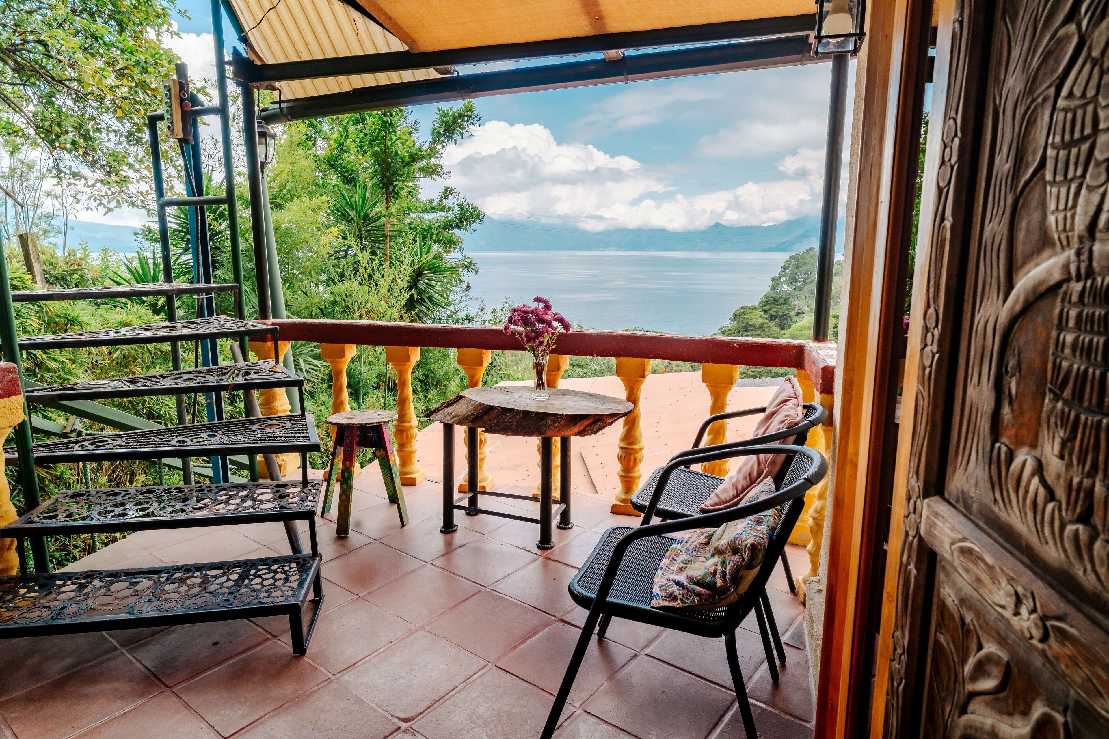 Un balcón con vista al mar, una mesa con un jarrón de flores y dos sillas.