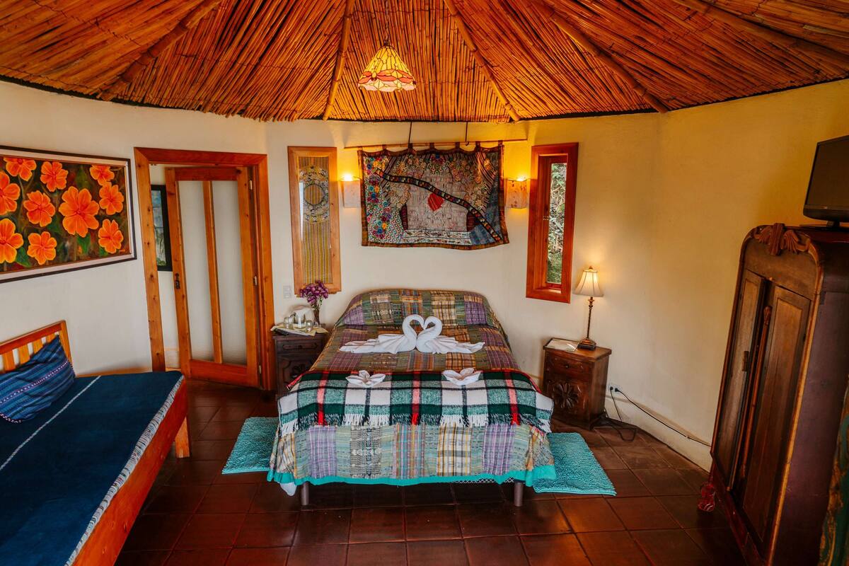 A room with a bed, a sofa, a wooden ceiling, a wall tapestry, and a television.