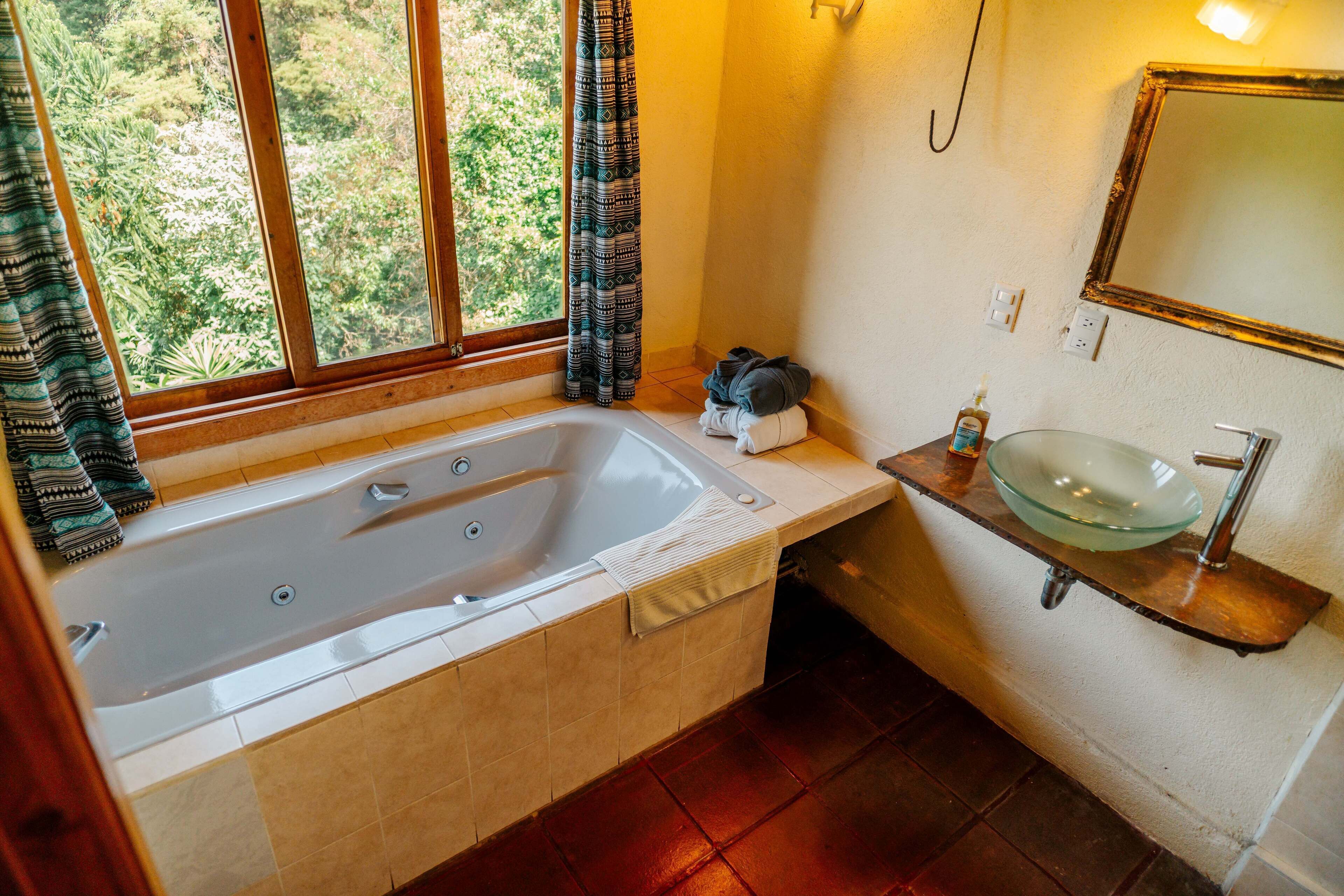 Ein Badezimmer mit Badewanne, Waschbecken aus Glas und einem fenster mit Vorhängen.