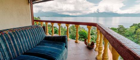 A balcony with a sofa, a railing, and a view of a lake and mountains.