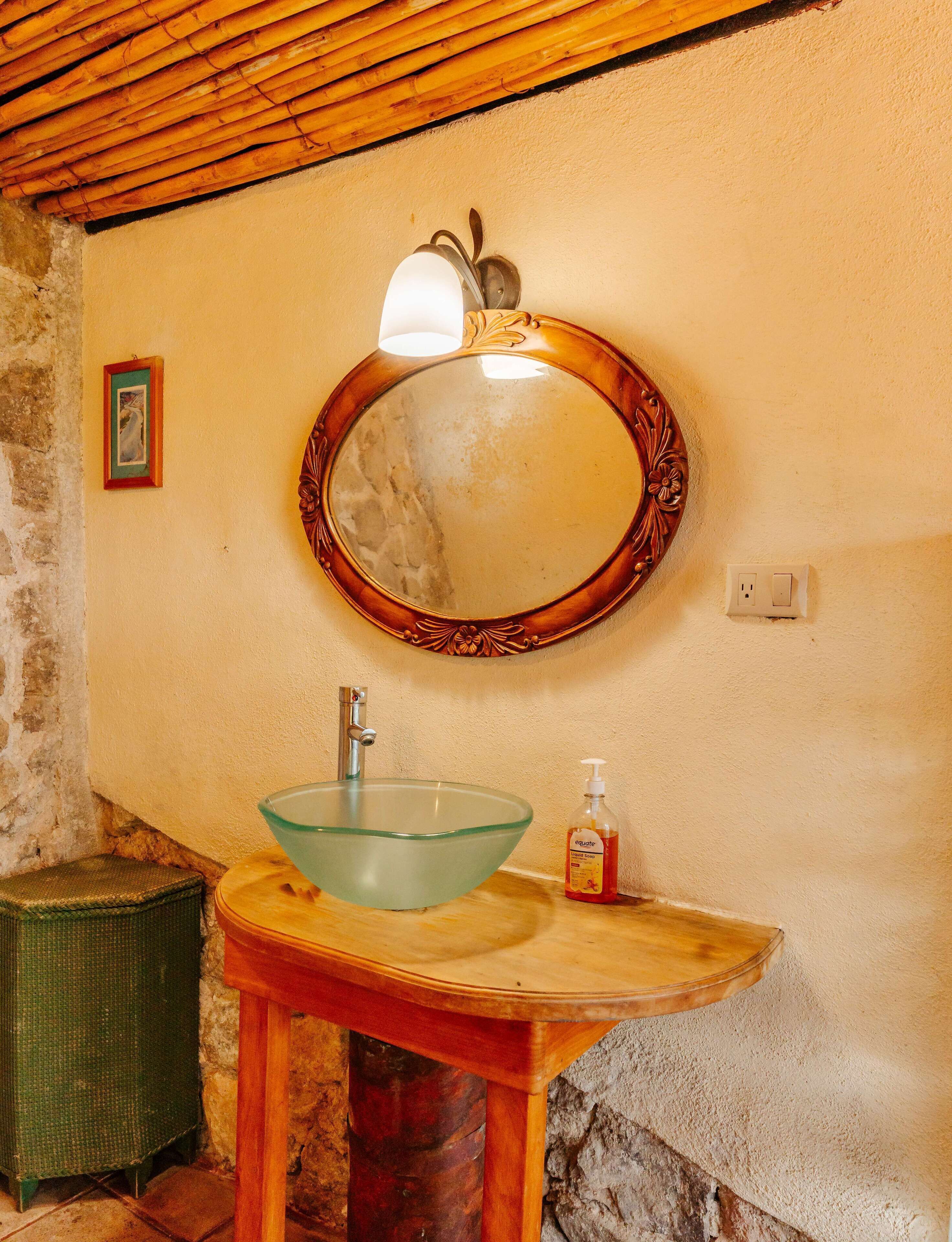 A bathroom with a wooden vanity, a glass sink, and a wall-mounted mirror with a decorative frame.