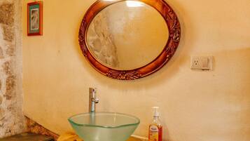 A bathroom with a wooden vanity, a glass sink, and a wall-mounted mirror with a decorative frame.