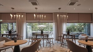 Un comedor moderno con mesas y sillas redondas, ventanas grandes con cortinas y vistas al exterior.