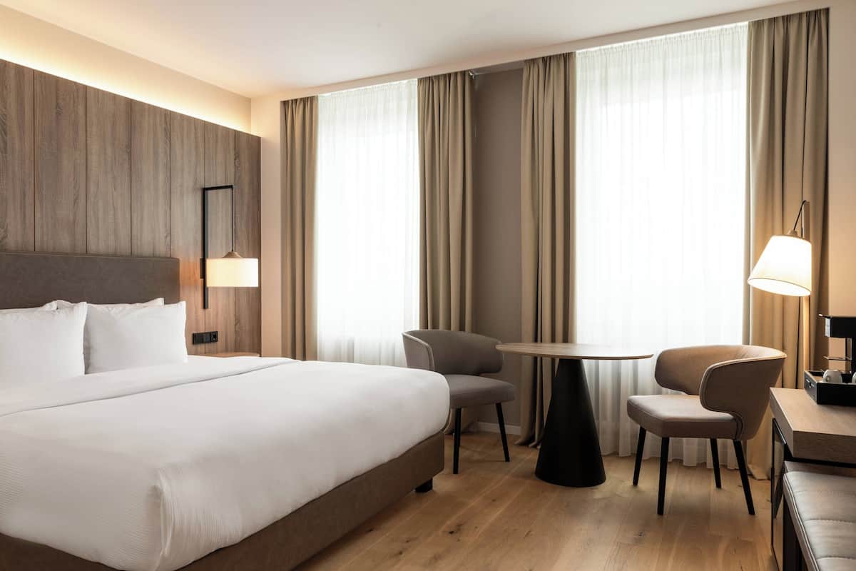 Una habitación de hotel con una cama grande, dos sillones, una mesita pequeña y un escritorio con una lámpara.