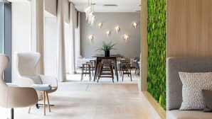 Un moderno vestíbulo de hotel con zona de comedor, área de estar con sofá y una pared decorativa verde.