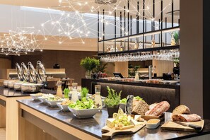A buffet with various food items and a bar area with glasses and bottles. - AC Hotel by Marriott Berlin Humboldthain Park (Berlin)