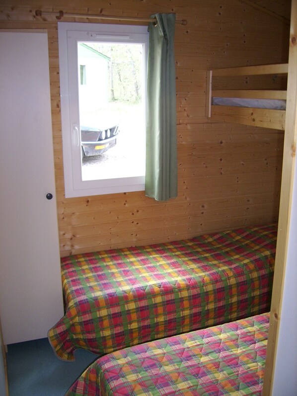 A small cabin with two bunk beds, a window with a curtain, and a door.