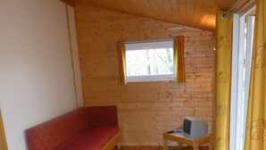 A small cabin with a wooden interior, a red sofa, a small table, and a window with curtains. - Ferme-Auberge des Trouilles (Lafrancaise)