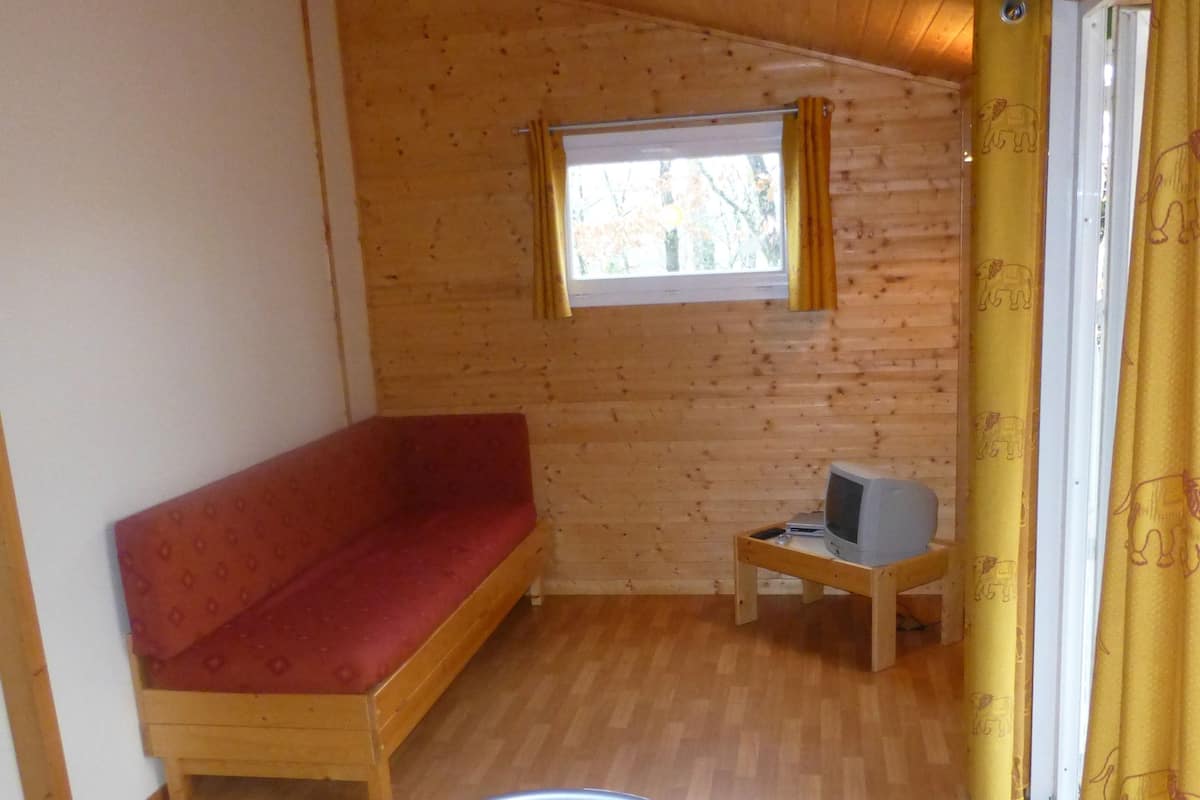 Une petite cabane avec un intérieur en bois, un canapé rouge, une petite table et une fenêtre avec des rideaux.