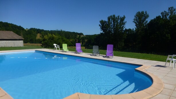 A rectangular swimming pool with a curved edge, surrounded by a tiled deck. - Ferme-Auberge des Trouilles (Lafrancaise)