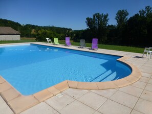 A rectangular swimming pool with a curved edge, surrounded by a tiled deck.