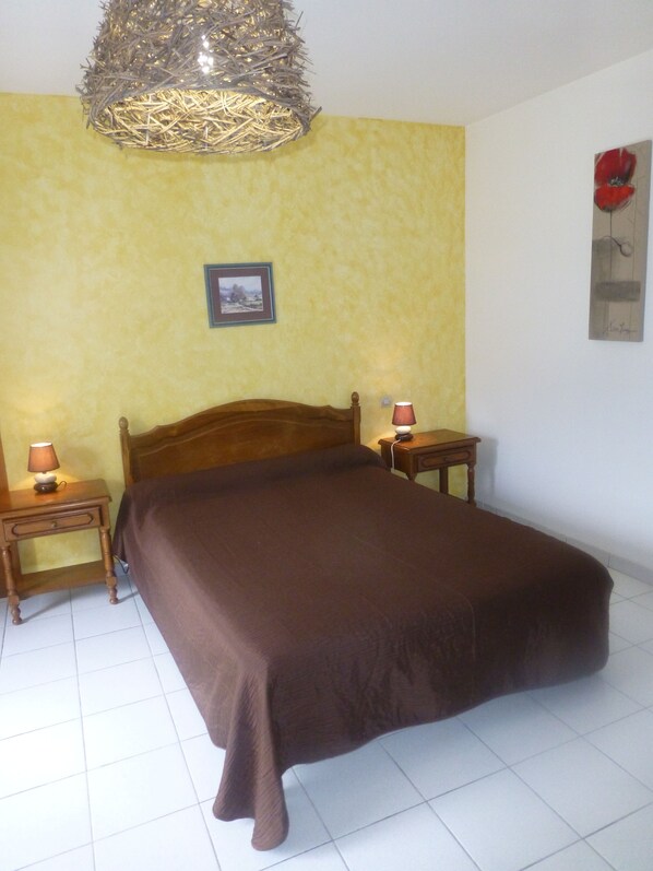 A bedroom with a wooden bed, two bedside tables with lamps, a framed picture on the wall, and a decorative hanging light fixture.