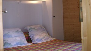 A small, single-bed room with a wooden ceiling and walls, a colorful bedspread, and a wall-mounted light fixture. - Ferme-Auberge des Trouilles (Lafrancaise)